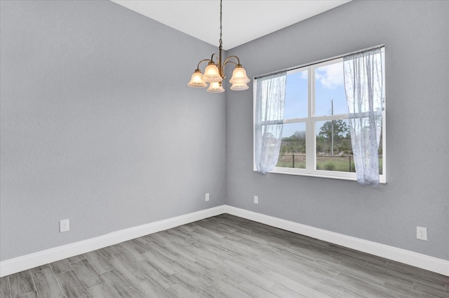 spare room with wood finished floors, a notable chandelier, and baseboards