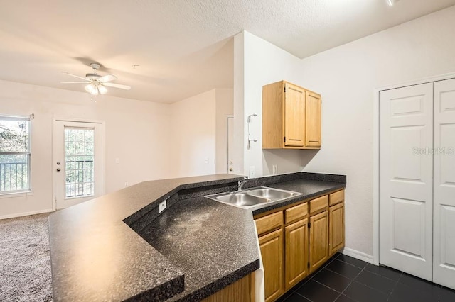 kitchen featuring a ceiling fan, dark tile patterned flooring, dark countertops, a peninsula, and a sink