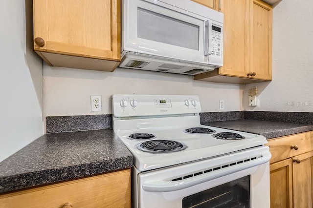 kitchen featuring dark countertops, white appliances, and light brown cabinetry