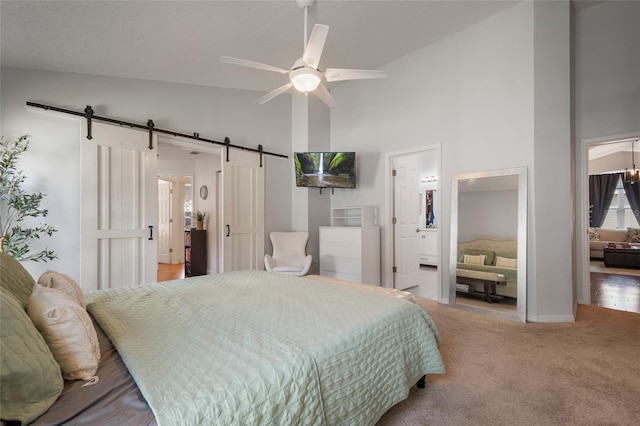 bedroom with high vaulted ceiling, ensuite bathroom, a barn door, carpet, and ceiling fan