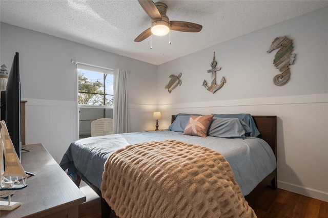 bedroom featuring ceiling fan, a textured ceiling, wood finished floors, and wainscoting