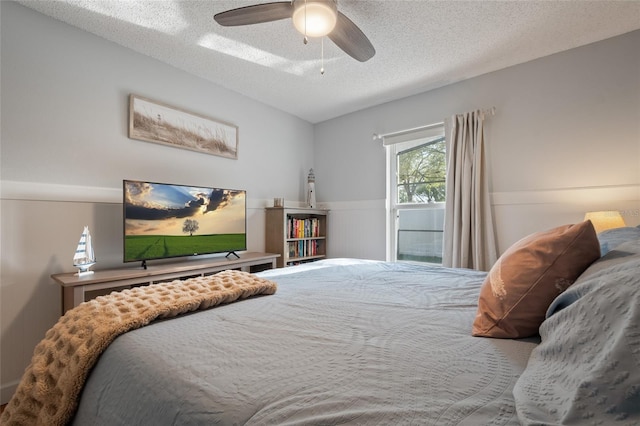 bedroom featuring a textured ceiling, ceiling fan, and wainscoting