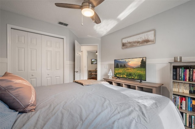 bedroom featuring a wainscoted wall, visible vents, a closet, and ceiling fan