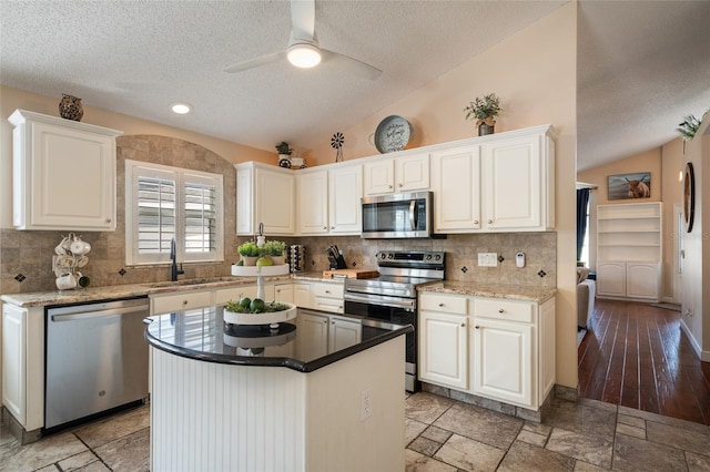 kitchen with vaulted ceiling, appliances with stainless steel finishes, white cabinetry, and a sink