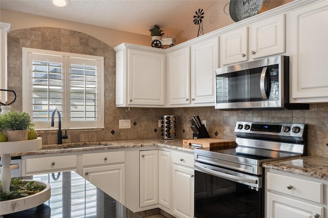 kitchen with a sink, tasteful backsplash, a textured ceiling, white cabinetry, and appliances with stainless steel finishes