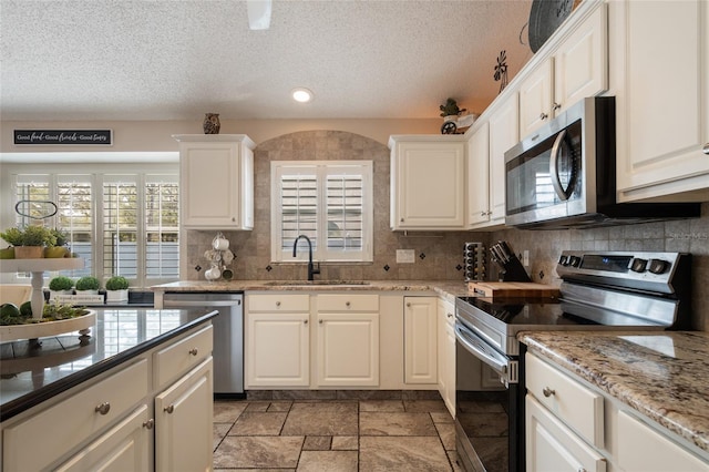 kitchen with tasteful backsplash, appliances with stainless steel finishes, stone tile flooring, white cabinetry, and a sink