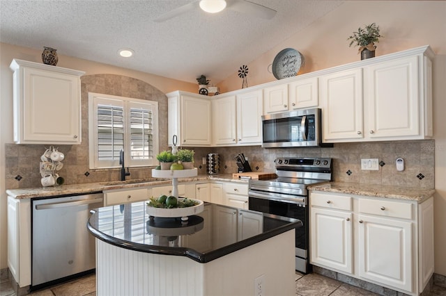 kitchen with a sink, stainless steel appliances, vaulted ceiling, white cabinets, and backsplash