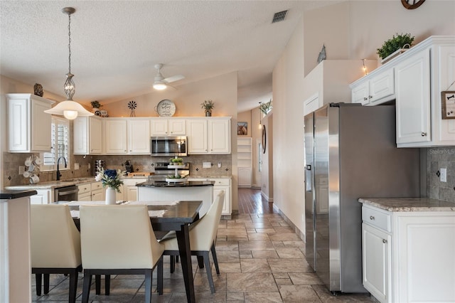 kitchen with tasteful backsplash, visible vents, a center island, stone tile flooring, and stainless steel appliances