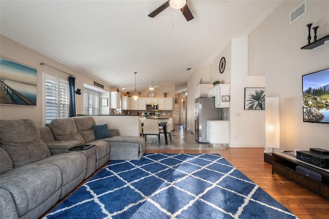 living room featuring visible vents, baseboards, ceiling fan, wood finished floors, and high vaulted ceiling