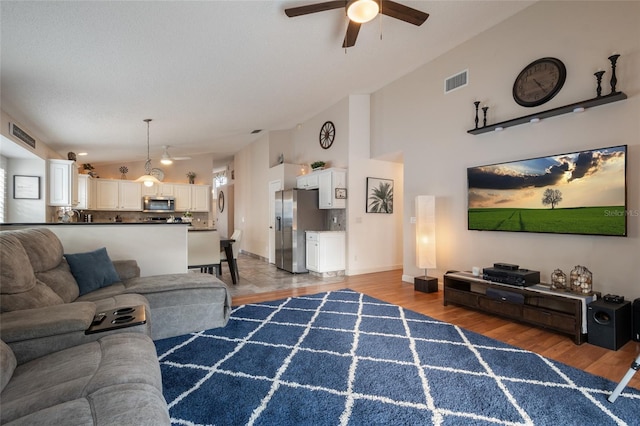 living area with vaulted ceiling, light wood-style flooring, a ceiling fan, and visible vents