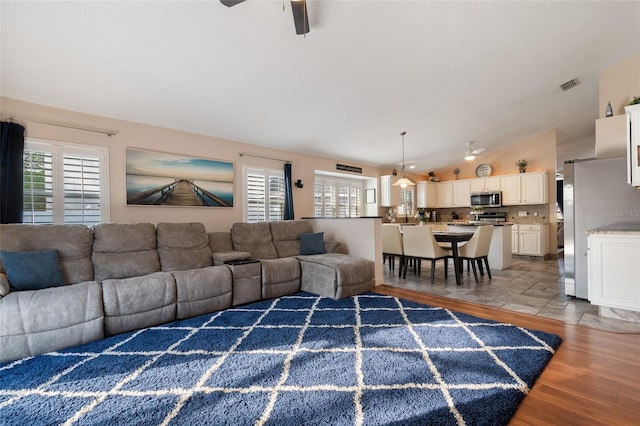 living room featuring visible vents, lofted ceiling, light wood-style flooring, and a ceiling fan