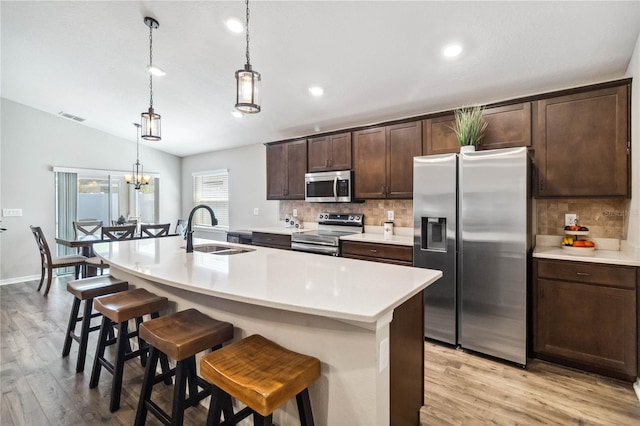 kitchen featuring visible vents, a sink, dark brown cabinets, appliances with stainless steel finishes, and a kitchen bar