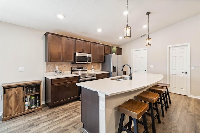 1575 Eucalyptus Way, Davenport, FL 33837 - kitchen with appliances with stainless steel finishes, vaulted ceiling, tasteful backsplash, light wood-style flooring, and an island with sink