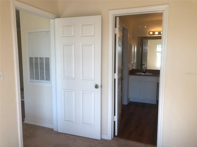 corridor featuring dark carpet, a sink, and baseboards