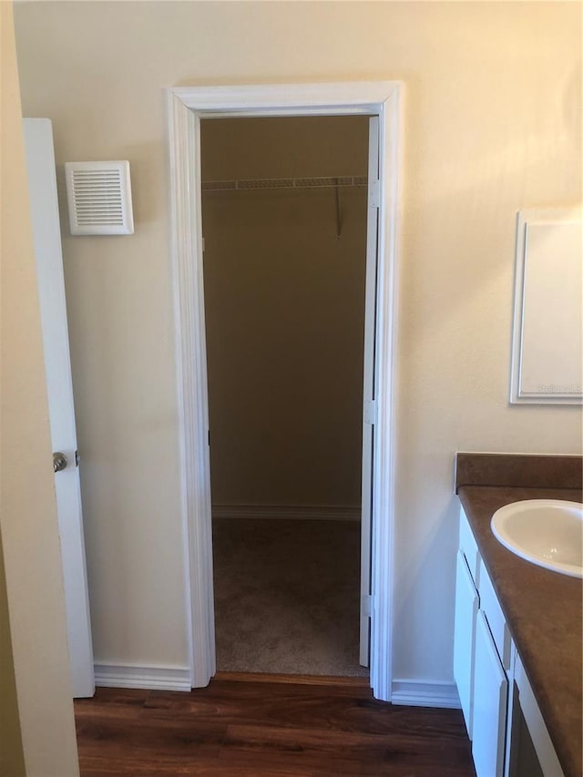 bathroom with wood finished floors, vanity, visible vents, baseboards, and a spacious closet