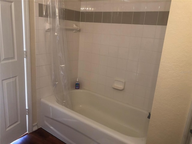 full bath featuring shower / tub combo, wood finished floors, and a textured wall