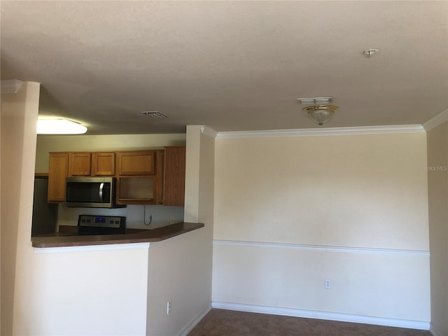 kitchen with baseboards, appliances with stainless steel finishes, brown cabinetry, dark countertops, and crown molding