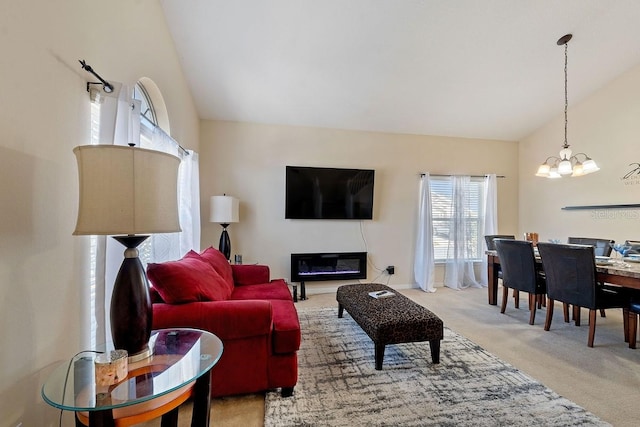 living area featuring light carpet, baseboards, a glass covered fireplace, high vaulted ceiling, and a notable chandelier