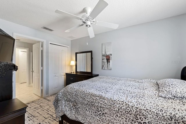 bedroom featuring a textured ceiling, ceiling fan, light tile patterned flooring, visible vents, and a closet