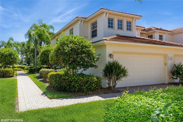 mediterranean / spanish home with an attached garage, a tiled roof, and stucco siding