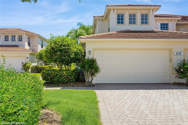 view of front of house featuring an attached garage, stucco siding, decorative driveway, and a tiled roof