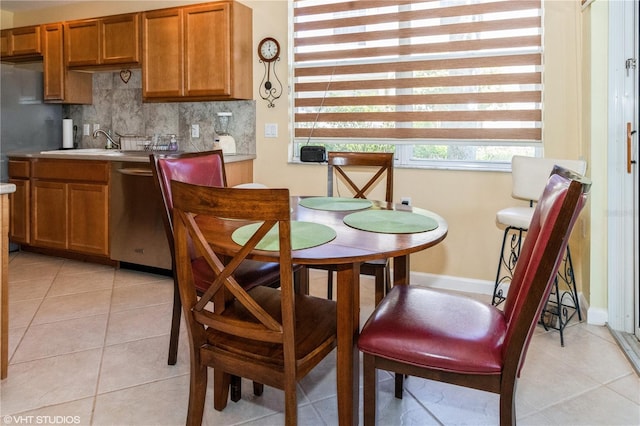 kitchen with light tile patterned floors, tasteful backsplash, brown cabinetry, stainless steel dishwasher, and a sink