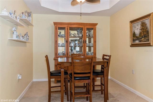 dining area with light tile patterned floors, a raised ceiling, and baseboards