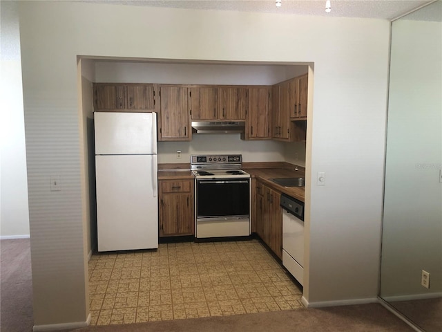 kitchen featuring brown cabinets, light floors, a sink, white appliances, and under cabinet range hood