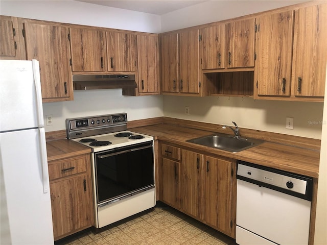 kitchen featuring under cabinet range hood, white appliances, a sink, light floors, and brown cabinetry