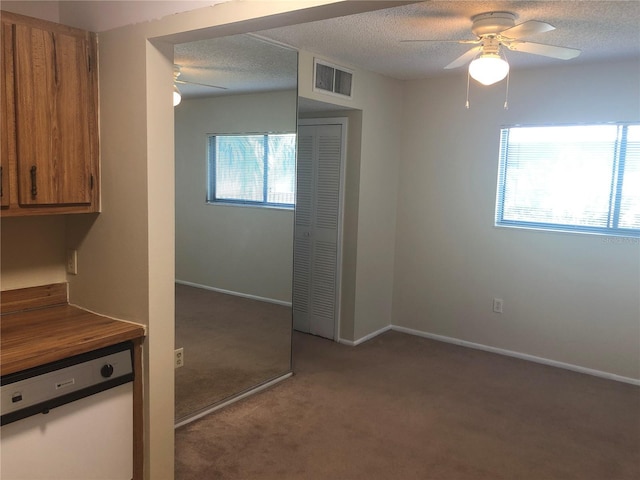 kitchen with carpet, brown cabinets, visible vents, white dishwasher, and a textured ceiling