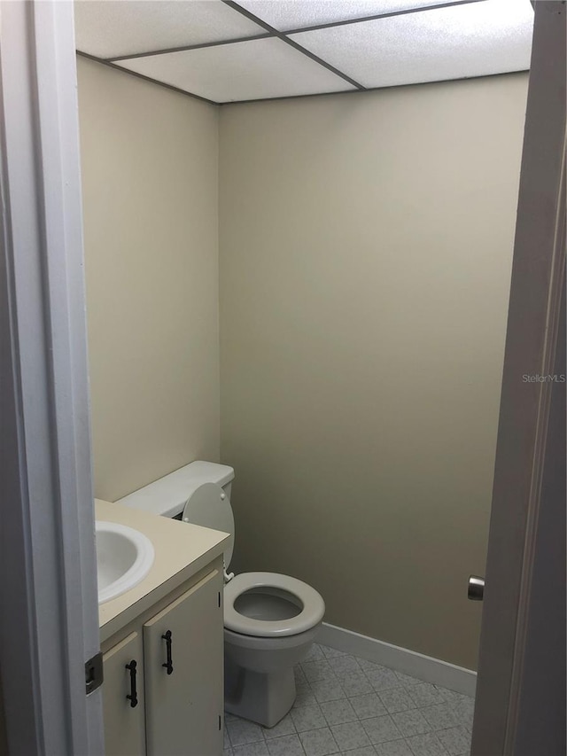 half bath featuring baseboards, toilet, tile patterned flooring, vanity, and a paneled ceiling