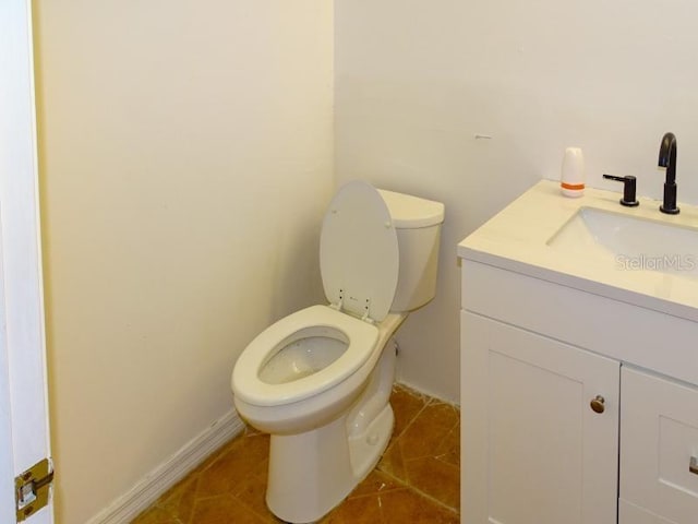 half bath with toilet, tile patterned flooring, baseboards, and vanity