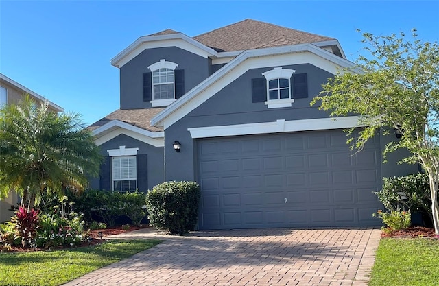 traditional-style house featuring stucco siding, a shingled roof, decorative driveway, and a garage