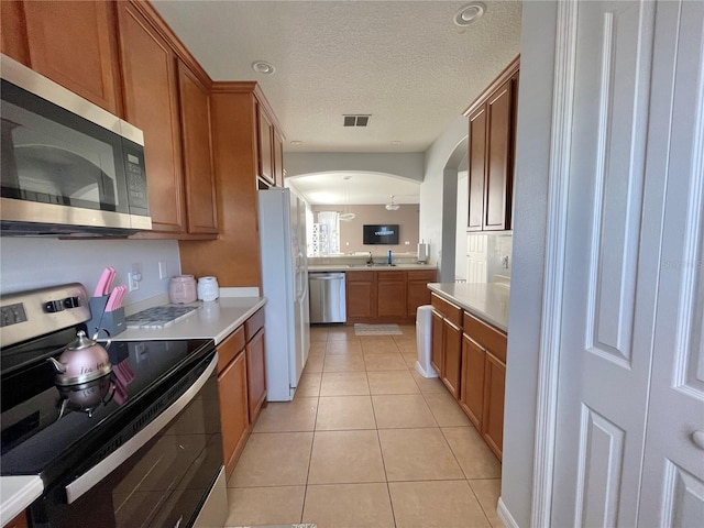 kitchen featuring visible vents, light tile patterned floors, appliances with stainless steel finishes, arched walkways, and brown cabinetry