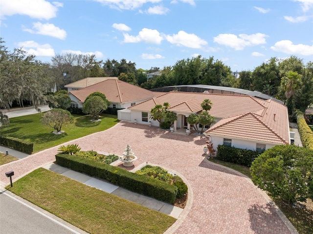 view of front of house with decorative driveway, a tile roof, a front lawn, and a lanai