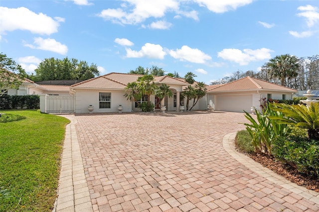 mediterranean / spanish-style house featuring a tiled roof, an attached garage, fence, decorative driveway, and a front yard