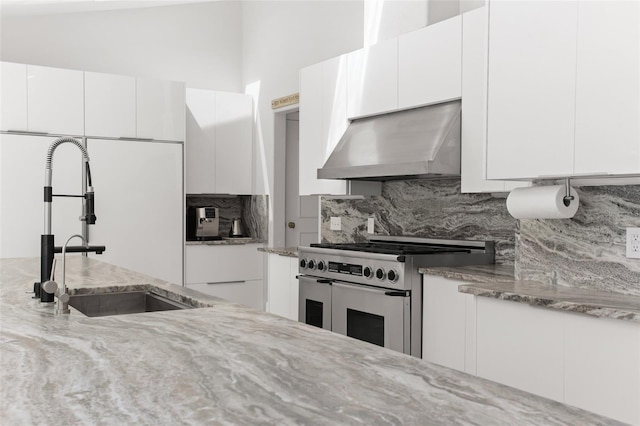 kitchen with range with two ovens, light stone counters, decorative backsplash, a sink, and extractor fan