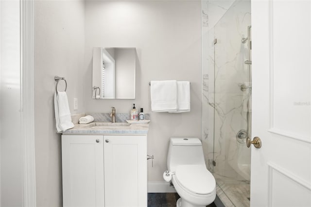 bathroom with toilet, a marble finish shower, baseboards, and vanity