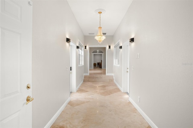 hallway featuring baseboards, arched walkways, and a notable chandelier