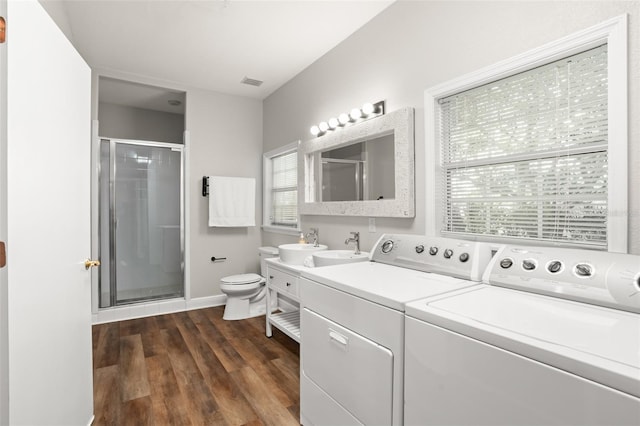 bathroom featuring washer and clothes dryer, double vanity, toilet, a stall shower, and wood finished floors