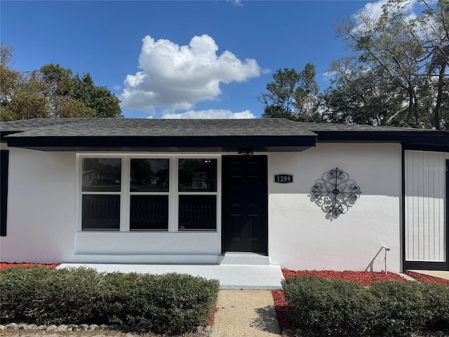 entrance to property featuring roof with shingles and stucco siding