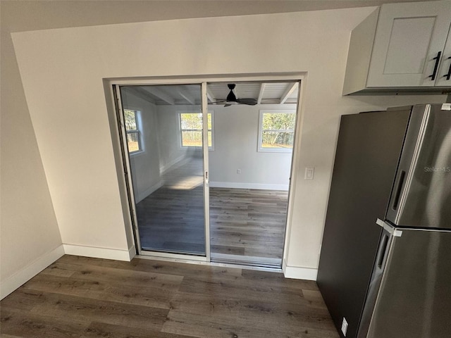 unfurnished dining area with ceiling fan, dark wood-style flooring, beam ceiling, and baseboards