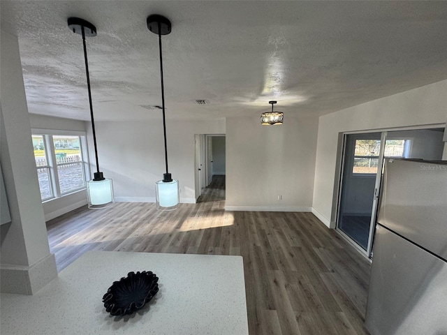 unfurnished living room with a textured ceiling, wood finished floors, visible vents, and baseboards