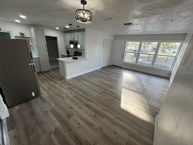 kitchen featuring a peninsula, wood finished floors, visible vents, baseboards, and appliances with stainless steel finishes