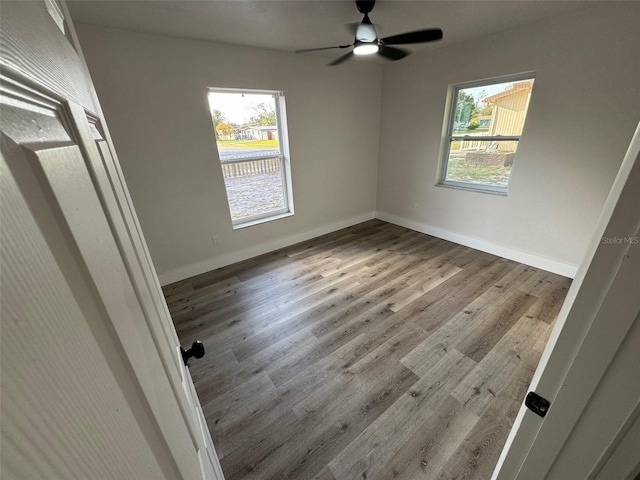 unfurnished bedroom with ceiling fan, multiple windows, wood finished floors, and baseboards