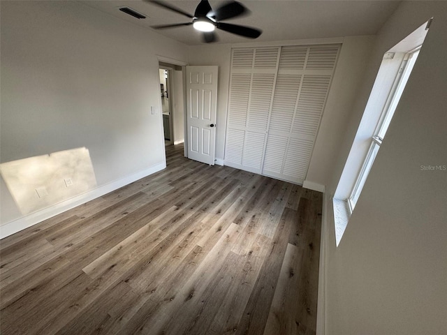 unfurnished bedroom with baseboards, visible vents, ceiling fan, wood finished floors, and a closet