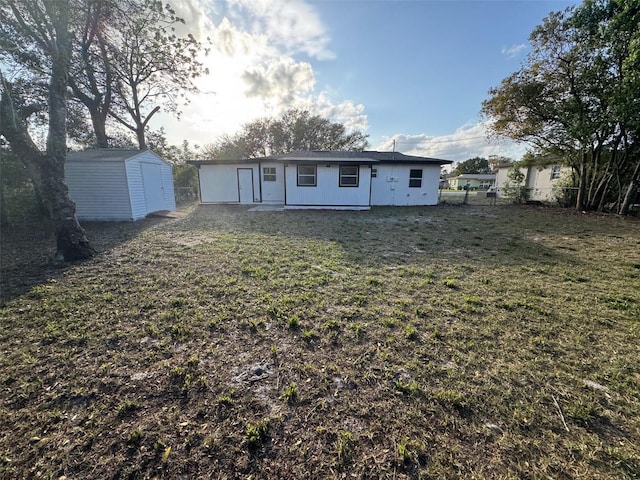 back of house featuring fence, a lawn, an outdoor structure, and a storage unit