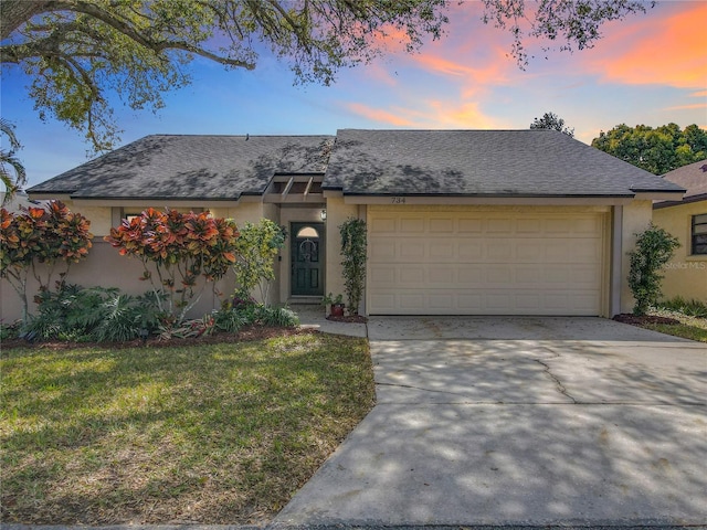 view of front facade featuring stucco siding, a shingled roof, a front yard, a garage, and driveway