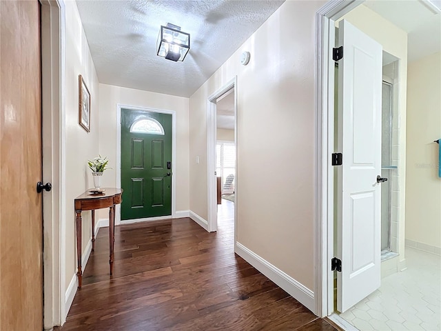 foyer entrance with a textured ceiling, dark wood-style floors, and baseboards