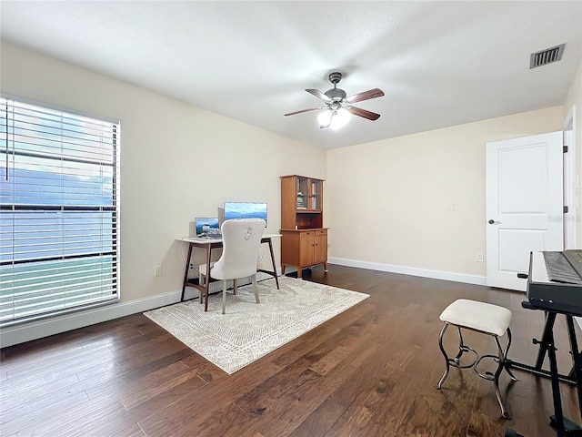 home office featuring dark wood-type flooring, a ceiling fan, visible vents, and baseboards